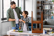 © Syda Productions - family, diy and home improvement concept - happy smiling father and son in gloves restoring old table and making fist bump gesture at home