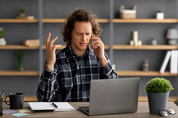 Poster - Displeased Businessman Talking On Cellphone Sitting At Laptop At Workplace