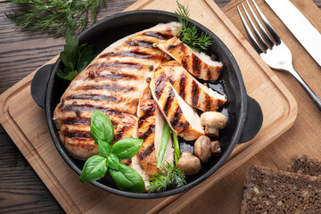 Wall Mural - Roasted chicken fillet and mushrooms with herb in the frying pan on the wooden table close-up.