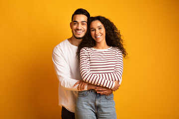 Wall Mural - Portrait of cheerful young arab couple embracing and smiling at camera