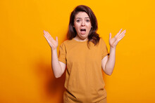 Frightened Person Showing Shocked Facial Expression, Standing Over Orange Background. Anxious Woman Feeling Scared And Terrified While Looking At Camera. Panicked Adult With Hands Up