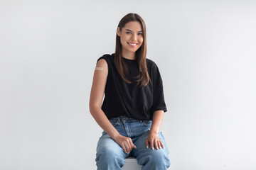 Wall Mural - Portrait of happy vaccinated woman with plaster bandage on her arm after covid-19 vaccine injection on light background