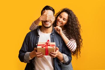 Wall Mural - Surprise Present. Romantic young arab woman covering boyfriend's eyes and giving gift