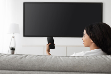 Poster - Smart home. Excited african american woman with cellphone connected to TV, plasma television with empty screen, mockup
