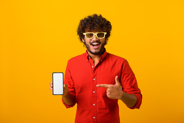 Happy cheerful beaded man pointing finger at smartphone with empty screen looking at camera with toothy smile, freespace for adv. Indoor studio shot isolated on orange background