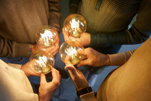 Team Of Four Intelligent People Together Holding Bright, Shining, Glowing Edison Light Bulbs As Symbol Of Implementing Innovations And Developing Modern, Creative, Clever Ideas, Close Up, Closeup Shot