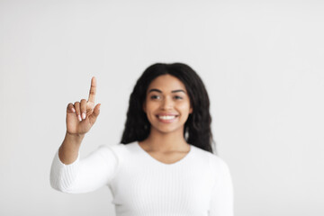 Smart home. Young african american lady pointing finger in the air pushing button on invisible screen