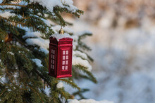Christmas Bauble, Red Telephone Box Shaped Ornament Hung On A Christmas Tree Covered With Snow. Winter Season And Festive Atmosphere. 