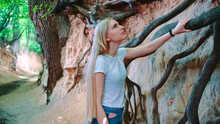 Young Blonde Woman Looking On Exposed Tree Roots In Natural Loess Ravine. Zoom Shot