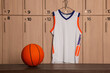 Orange basketball ball on wooden bench and hanger with uniform in locker room