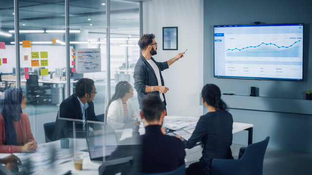 Fototapete - Diverse Modern Office: Motivated Businessman Leads Business Meeting with Managers, Talks, uses Presentation TV with Statistics, Chart Growth, Big Data. Digital Entrepreneurs Work on e-Commerce Project