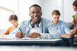 © Prostock-studio - Black male student sitting at desk writing in classroom
