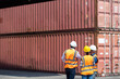 © NVB Stocker - Hispanic man harbor worker talking on the walkie-talkie radio and control loading containers at container warehouse. container yard port of import and export goods