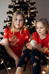 Wall Mural - Teenage sisters in red holiday T-shirts sitting at the Christmas tree and celebrating the New Year