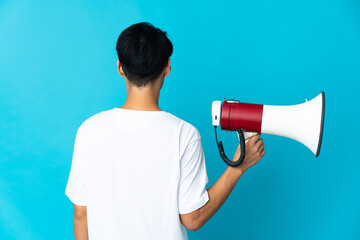 Poster - Young Chinese man isolated on blue background holding a megaphone and in back position