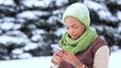 Portrait of beautiful attractive concentrated girl, young black African Afro American woman is looking at screen of her cell mobile phone, typing using smartphone at snowy winter day in snow hat scarf