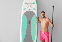 Sporty Man With Board For Sup Surfing And Oar On Light Background