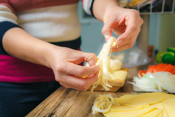 Young woman shredding cheese on a wooden table in kitchen