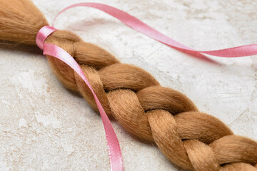 Braided red hair for donation with pink ribbon on grunge background, closeup