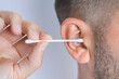 Closeup of man cleaning dirty ears with cotton swab or cotton stick. Ear cleaning and ear care