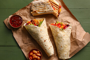 Tasty Mexican burritos with vegetables and sauce on green wooden background