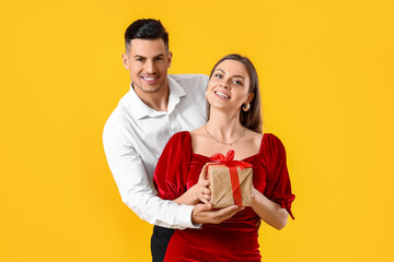 Poster - Happy young couple with gift on yellow background. Valentine's Day celebration