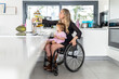 © Santi Nuñez/Stocksy - Wheelchair mother in the kitchen with daughter