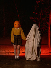 Pumpkin Headed Woman And Ghost Hold Hands At Night.