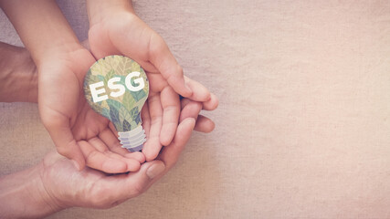 Hands holding ESG on paper cut out light bulb, Environmental social governance concept