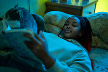 Teen Black Girl Reading A Book In Her Bedroom At Night.
