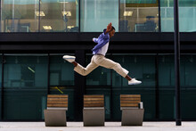 Stylish man dacing and jumping over street bench