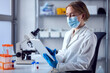 canvas print picture Female Lab Worker Wearing Lab Coat Working On Covid-19 Vaccine With Digital Tablet And Microscope