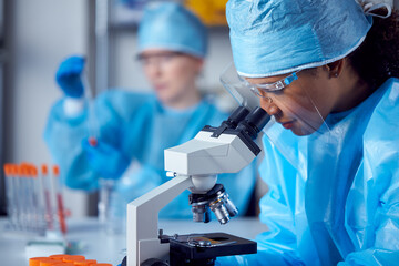 Female Lab Workers Wearing PPE Researching In Laboratory With Microscope