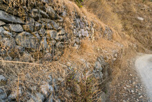A Roadside Stone Wall Covered With Moss And Dry Grass. These Type Of Stone Wall Are Generally Built In Mountain Regions To Avoid Landslides And Road Cutting.