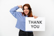 © luismolinero - Young redhead woman isolated on white background holding a placard with text THANK YOU and doing strong gesture
