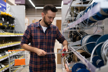 a man in a hardware store cuts off a metal cable with pliers