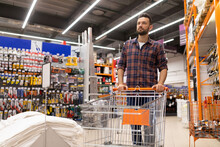 A Buyer At A Hardware Store With A Trolley Inspects The Rows With Goods Of Building Materials And Tools, The Concept Of Home Renovation And Housewarming, Shopping For Renovation