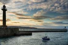 Sunset Over Whitby Harbour, Pier And Lighthouse As A Small Fishing Boat Comes Into The Harbour, Whitby, Yorkshire