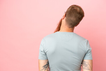 Wall Mural - Young reddish caucasian man isolated on pink background in back position and looking back