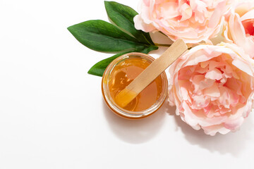 Liquid sugar paste for hair removal in a bowl with peony flower on white background.