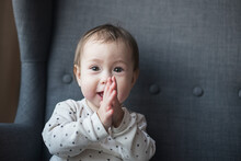 Portrait Of A 1 Year Old Baby With Brown Eyes And Two Teeth Clapping