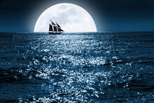 Very Large Full Blue Moon Rises Over This Ocean Scene As A Sailboat Quietly Saiils In Front Of It At A Distance, Completely Surrounded By The Moonrise