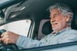 Happy owner. Handsome bearded mature man sitting relaxed in his newly bought car looking out the window smiling joyfully. One old senior driving and having fun..