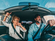 © Daniel - Couple of happy people dancing and singing in the car driving and traveling with a vehicle in the street enjoying their lifestyle having fun.