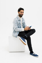 Young Man Sitting On Chair While Looking At Phone Celebrating On White Background