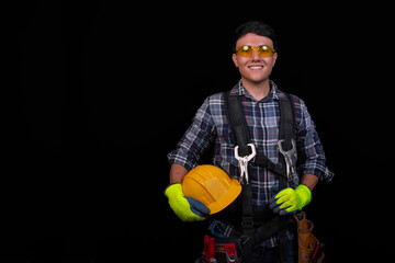 Young man smiling with his tools and safety equipment, on an isolated black background, copy paste, concept of safety at work