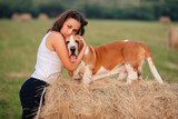Fototapeta Zwierzęta - A young adult girl walks with a Basset Hound dog in nature. The owner hugs the pet.