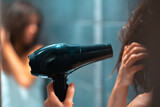 Girl is using hairdryer near the mirror, closeup.