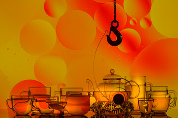 Wall Mural - transparent glass teapot and cups with tea and drops, silhouette of lifting hook on colorful background 