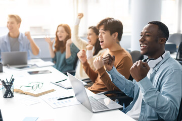 Group of excited people using laptop and shaking clenched fists